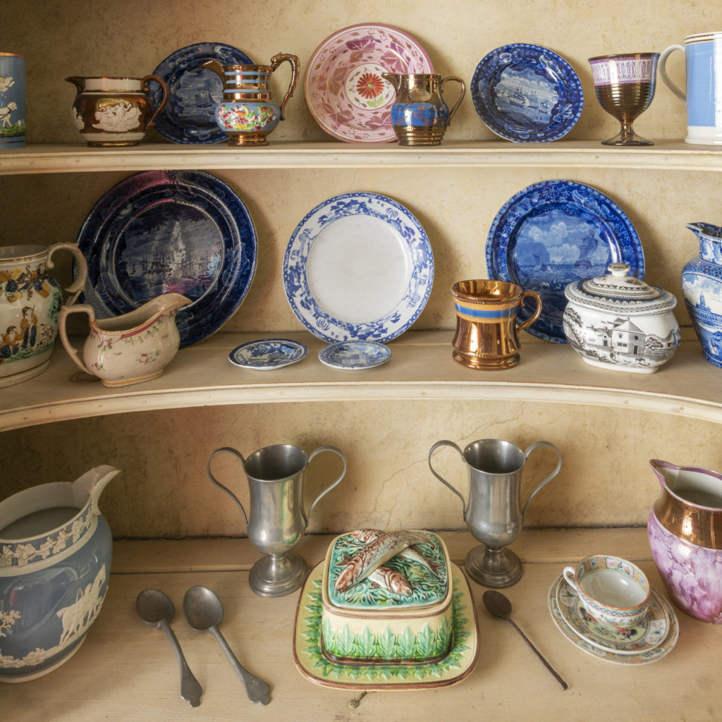 An open cabinet with four shelves of dishes in a variety of shapes and patterns.